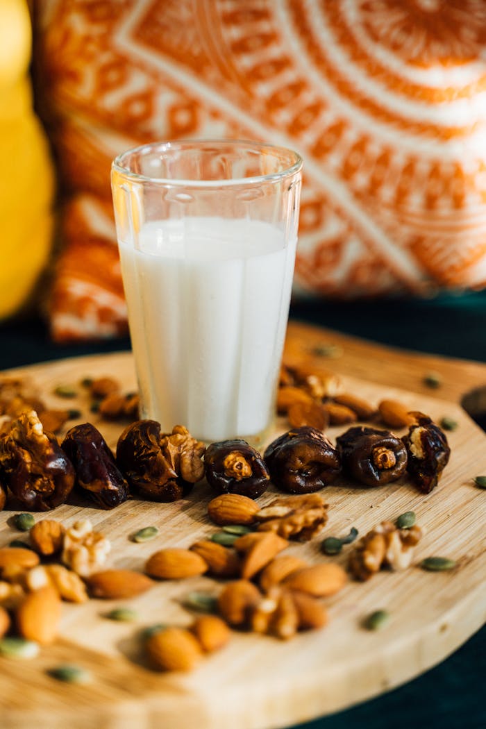 A glass of milk surrounded by dates and assorted nuts on a wooden board.